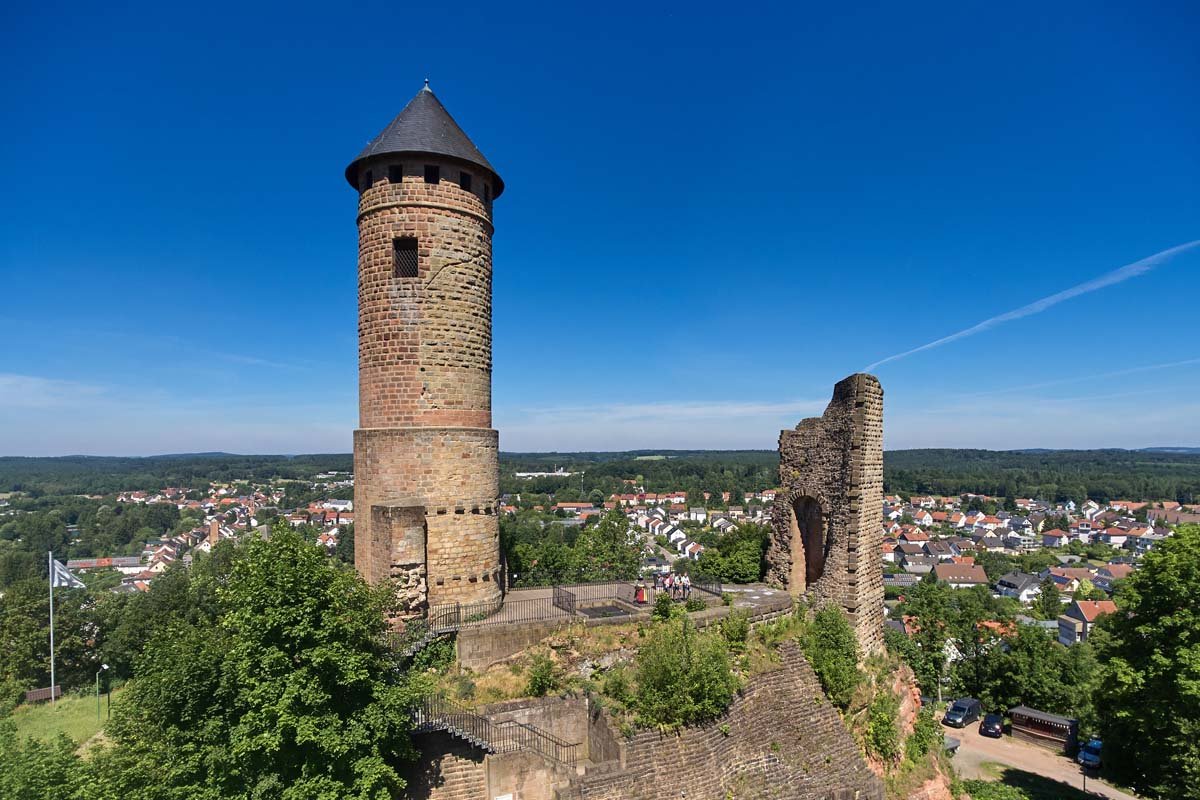 alter Burgturm mit einzelnen Gemäuern, Ort im Hintergrund