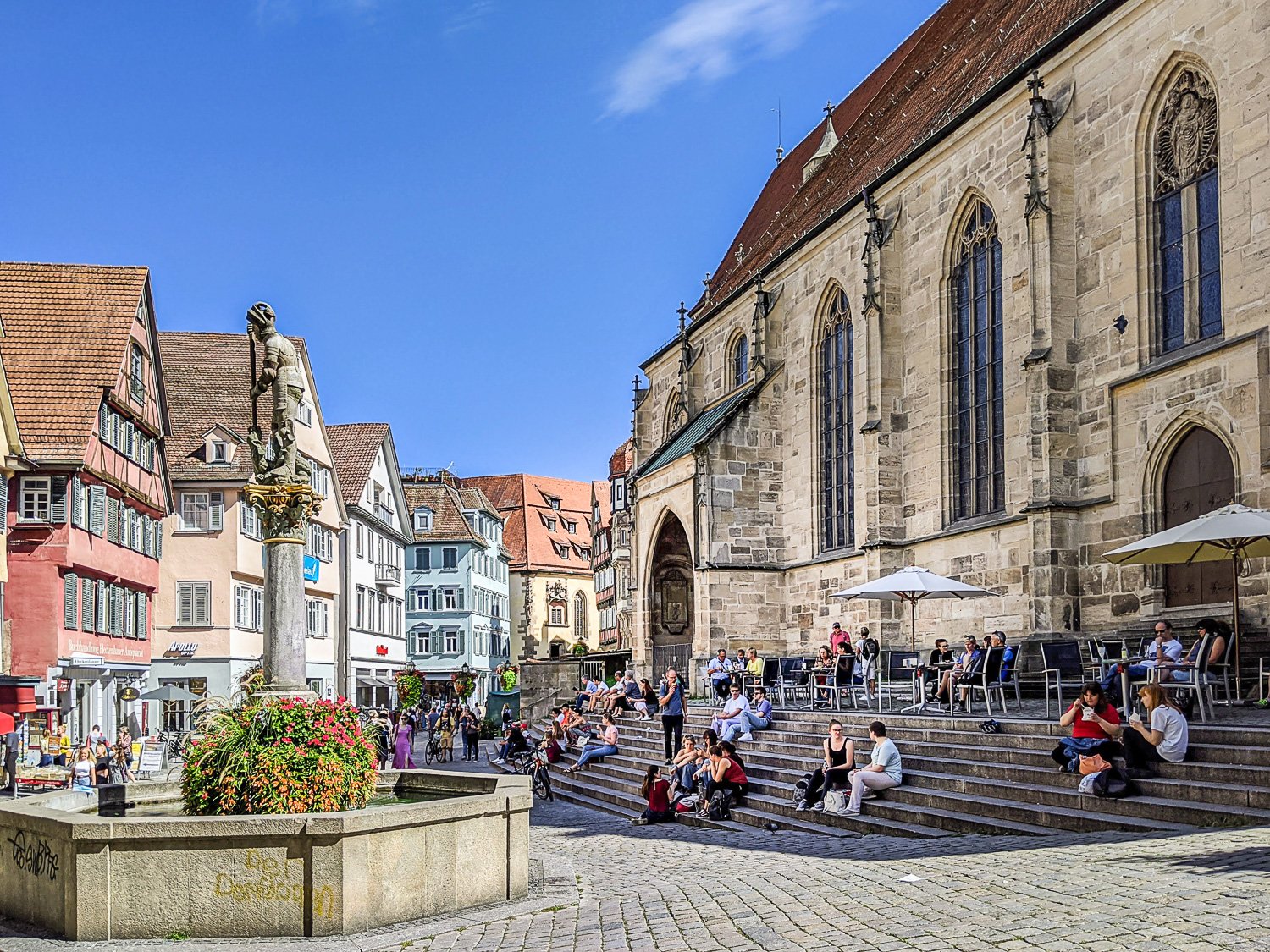 Holzmarkt mit St. Georgs-Brunnen und Passanten, die auf der Treppe vor der Stiftskirche verweilen