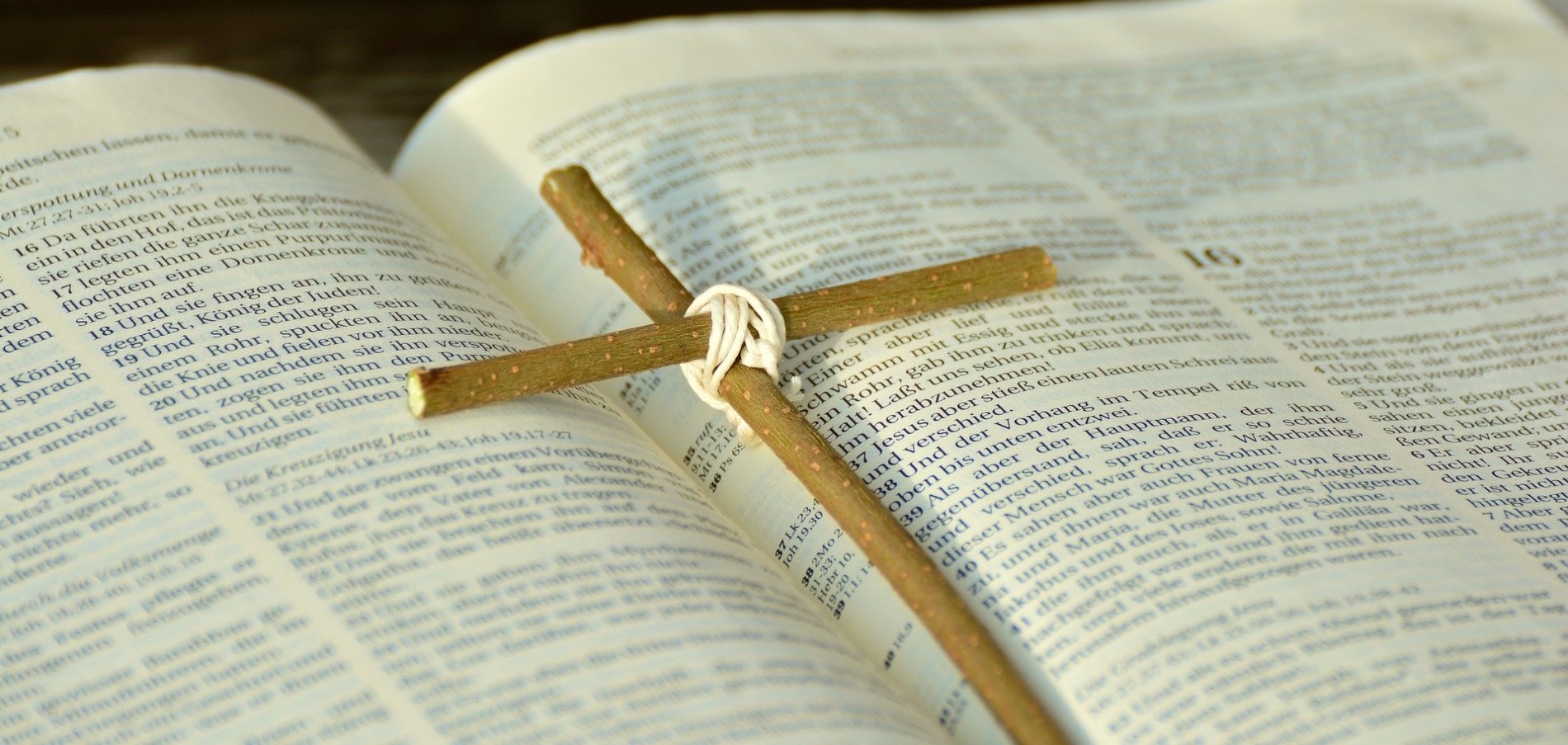 aufgeschlagene Bibel mit einem einfachen Holzkreuz aus zwei feinen Ästen darauf liegend