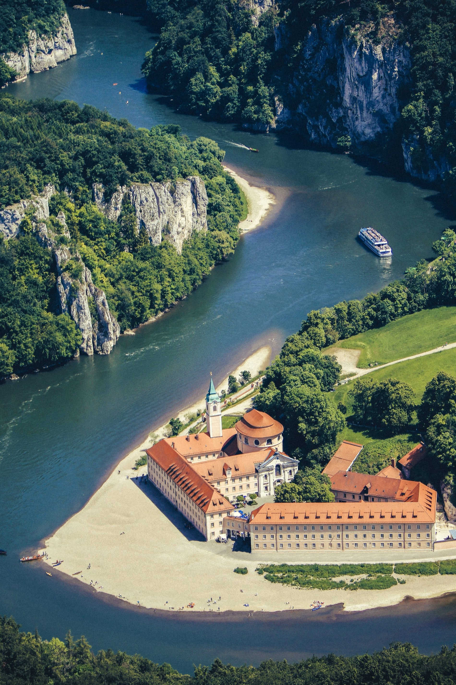 Kloster Weltenburg liegt an der Donau. Auf der Donau fahren ein Schiff und Boote. Die Donau schlängelt sich durch die mit Bäumen bewachsenen Felsen im Naturschutzgebiet Weltenburger Enge.