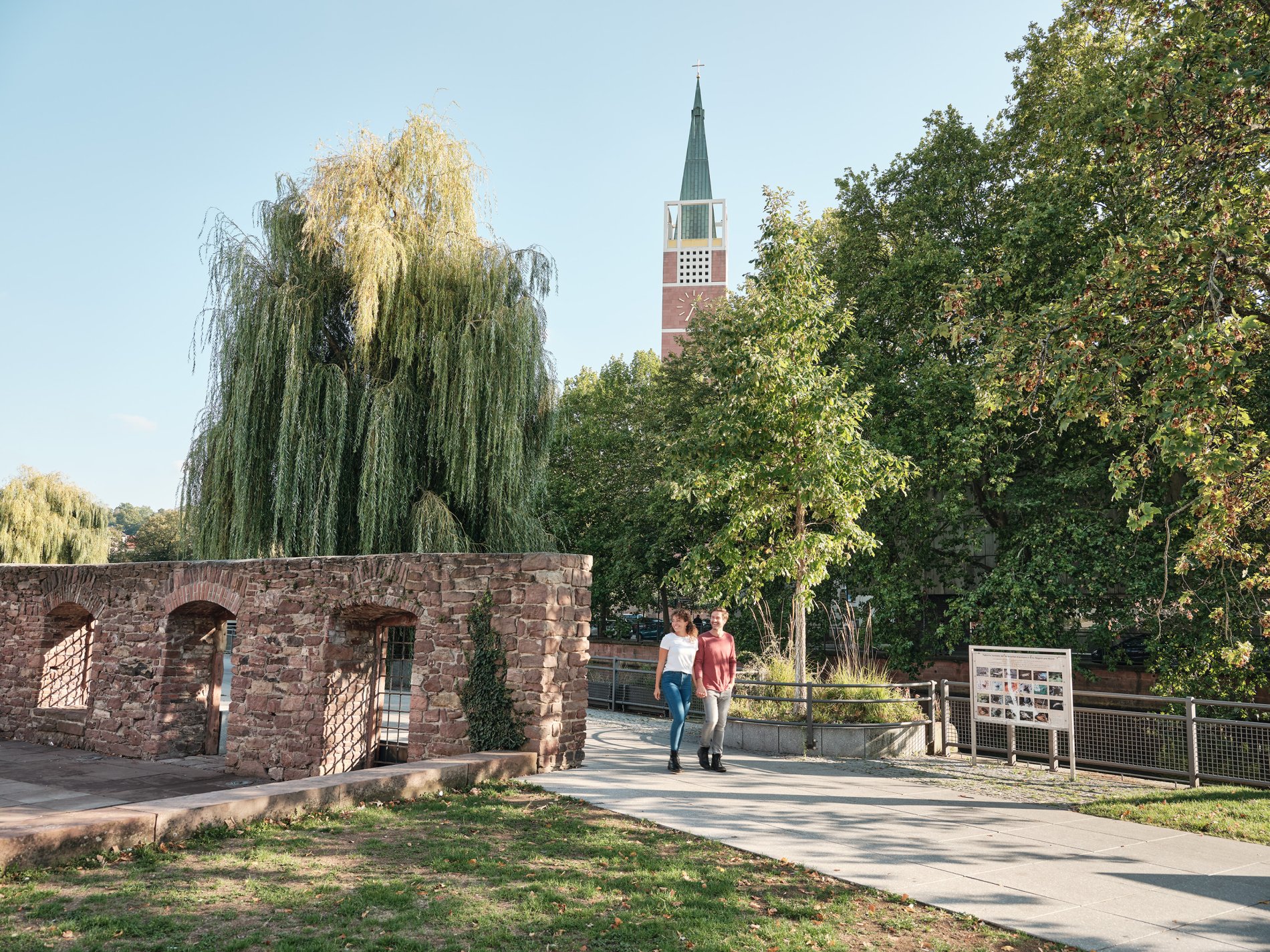 Spaziergehendes Paar mit Mauerresten an der Seite und Stadtkirche im Hintergrund.