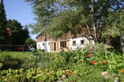 Biohofladen Maier in Münsingen im Biosphärengebiet Schwäbische Alb. Ein Bauernhaus mit Holz verkleidet. Im Vordergrund ein Blumenbeet und Bäume.