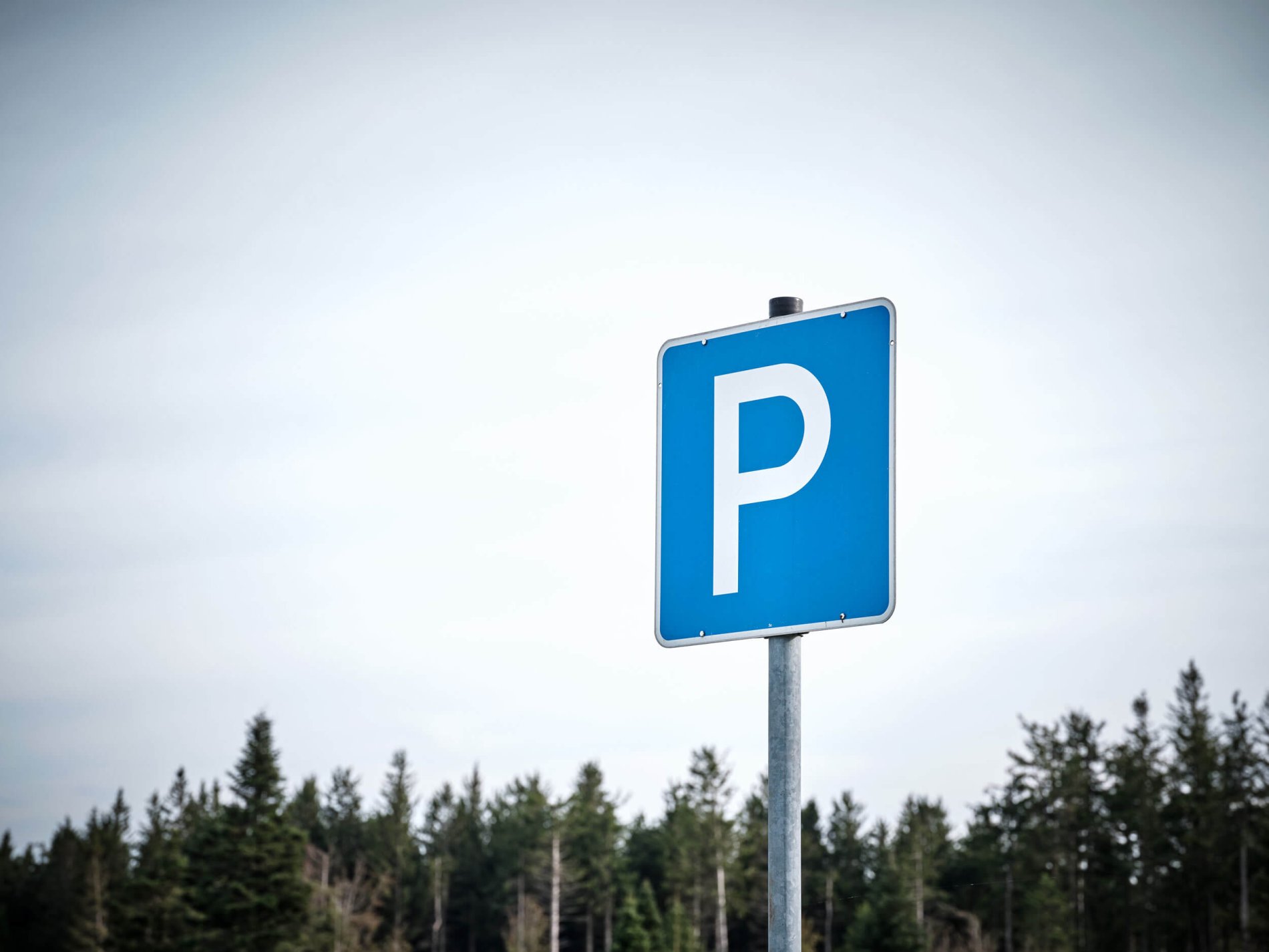 Ein blaues Parkplatzschild vor Wald und Himmel