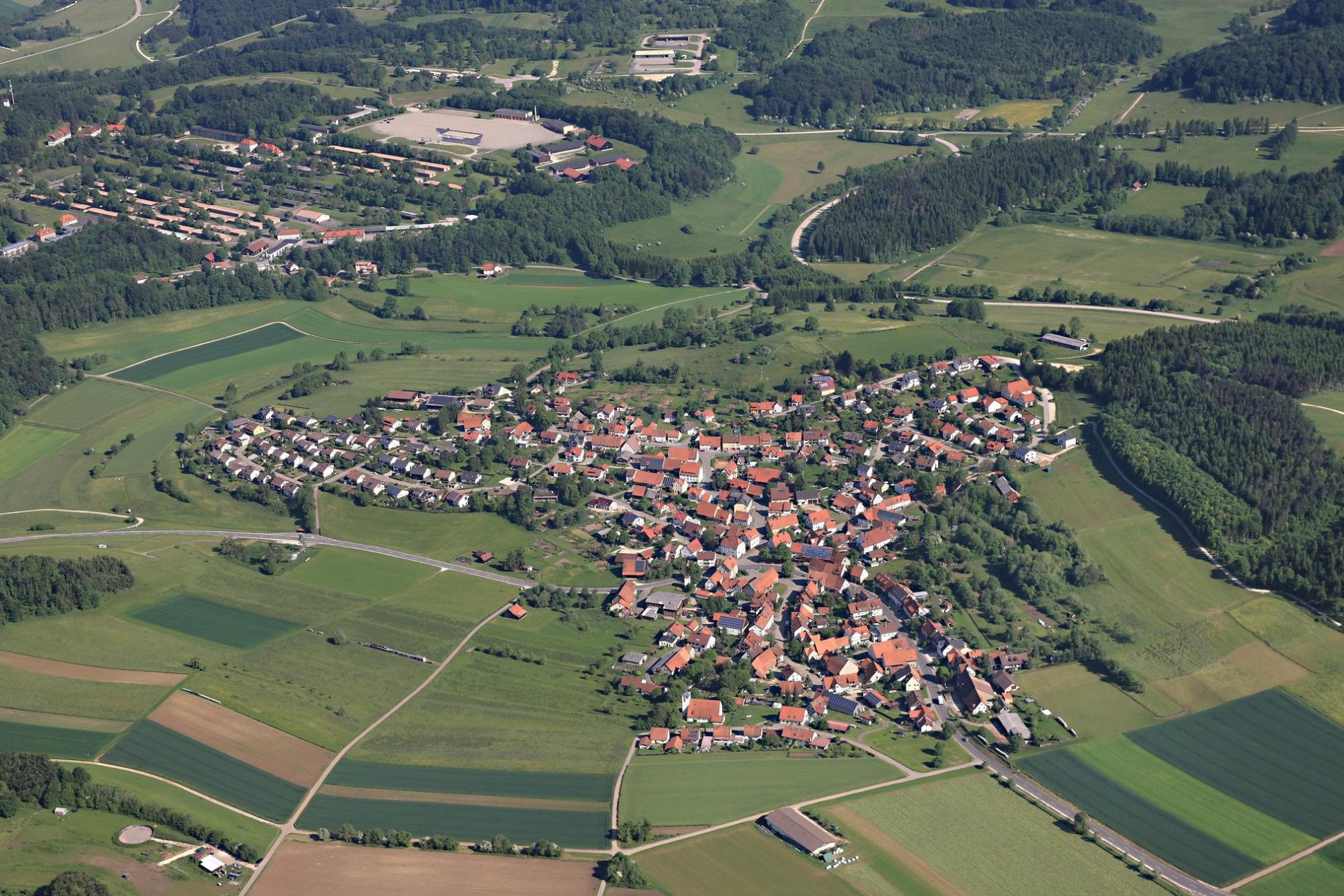 Ein Luftbild von einem Dorf. Ringsherum sind Felder und Wald.
