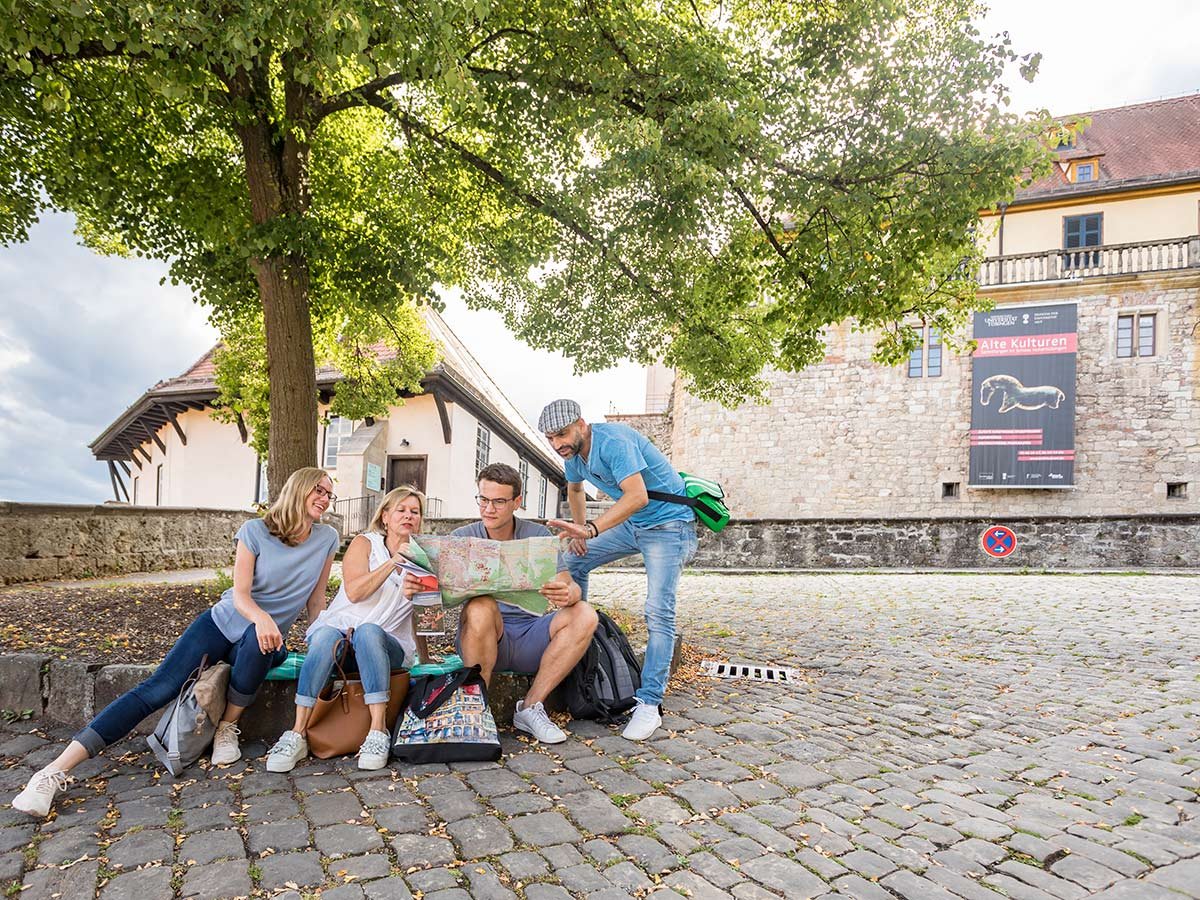Eine kleine Gruppe sitzt vor einem Baum im Vorhof des Museums Schloss Hohentübingen