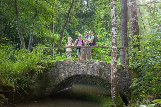 Eine Familie steht auf einer Steinbrücke über einem Bach.