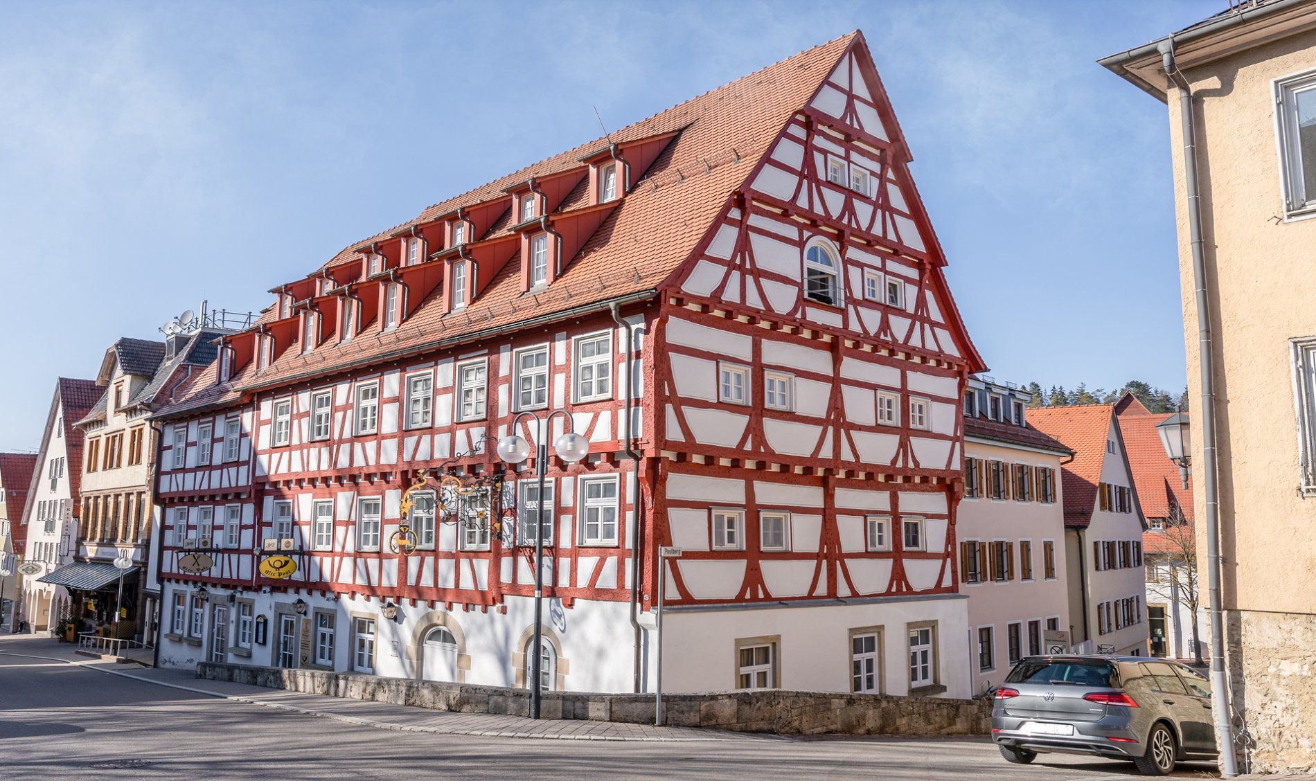 Gasthaus zum HIrsch und ehemalige Post in Münsingen im Biosphärengebiet Schwäbische Alb. Ein großes Fachwerkhaus in der Stadt direkt an einer Straße. An ihm hängt ein gelbes Postschild.