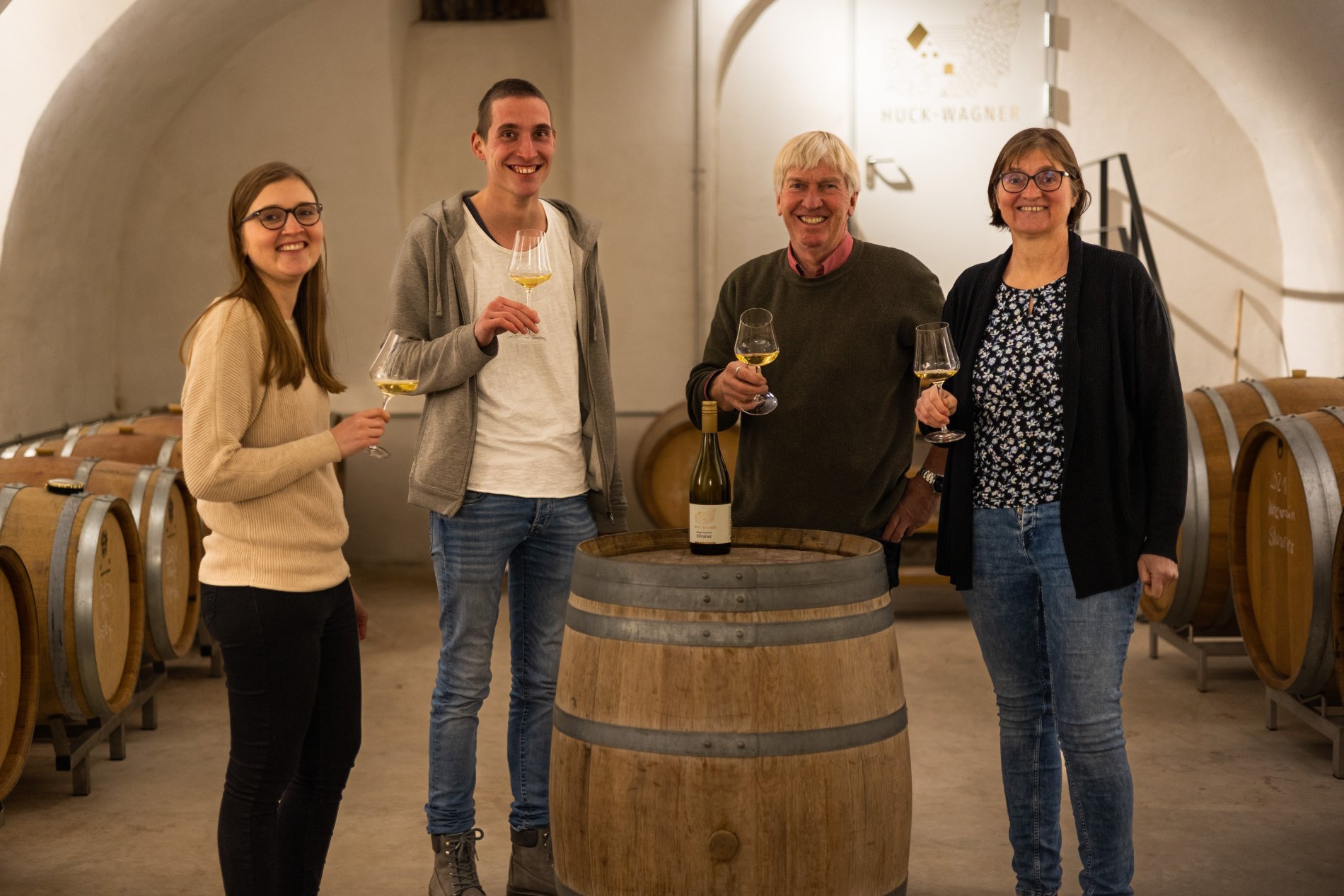 Famile Huck-Wagner steht gemeinsam im Gewölbekeller des Weinguts, ein Weißwein aus dem Tonneau wird verkostet.