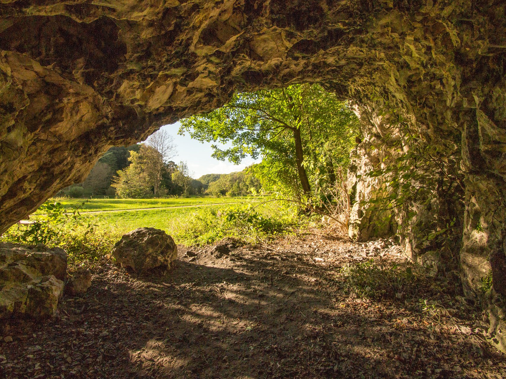 Geführte Themenführung "Wir erforschen eine Höhle" im Großen Lautertal im Biosphärengebiet Schwäbnische Alb. Ein kelienr Höhleneingang. Draußen ist es sonnig und die Wiesen und Bäume sind saftig grün.