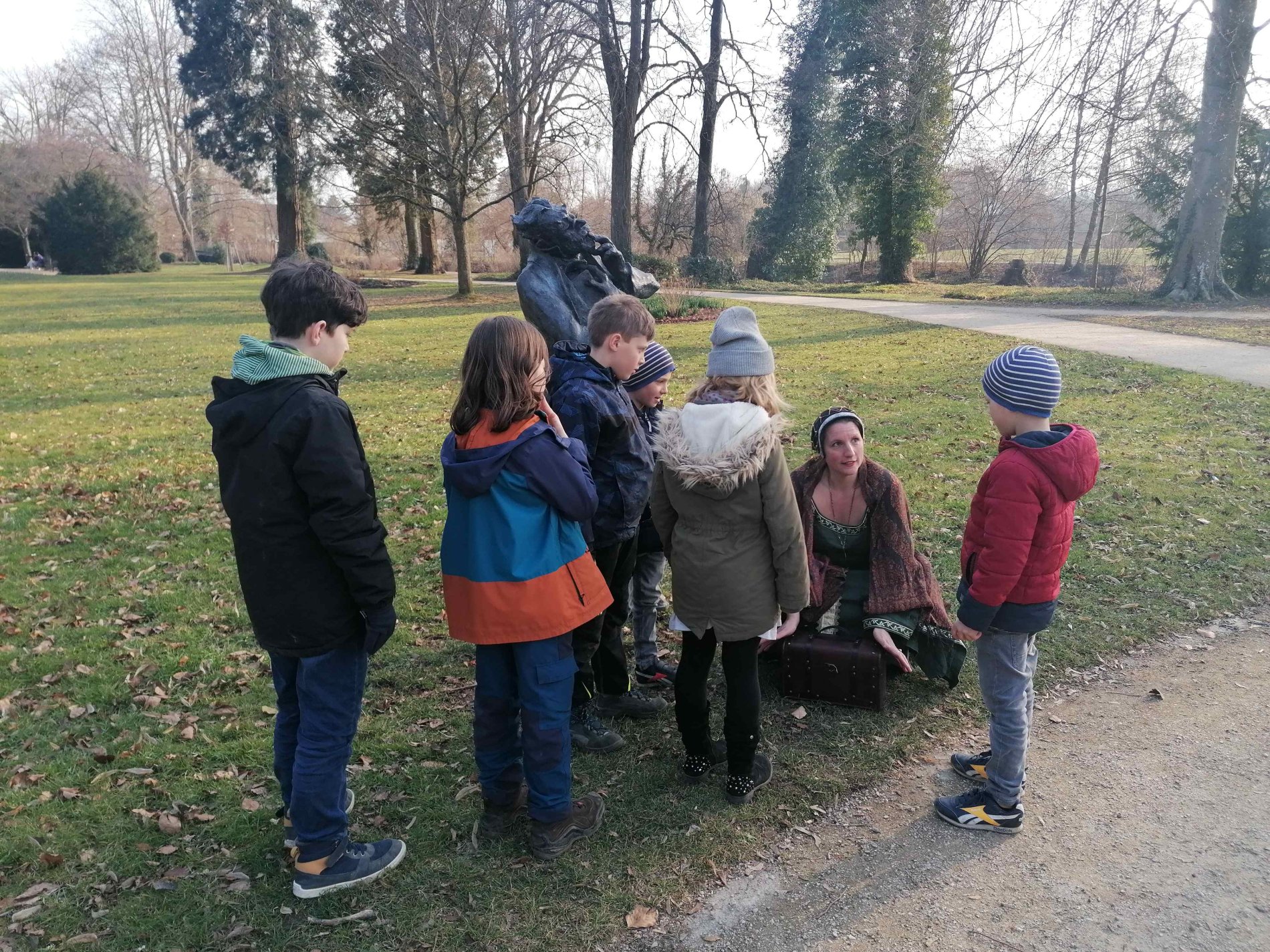 Herzogin Hadwig sitzt vor der Scheffelstatue im Stadtpark und erklärt den Kindern, was sie sehen.