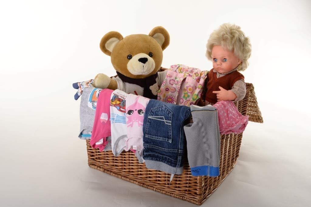 Teddybär, Puppe und Kleidung in einer Kiste