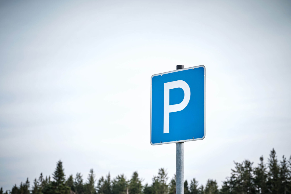 Ein blaues Parkplatzschild vor Wald und Himmel