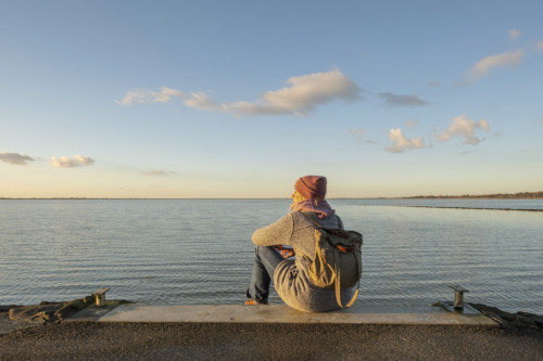 Frau sitzt an der Nordsee und blickt aufs Meer