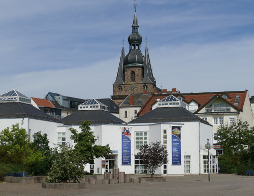 Das Mia-Münster-Haus in St. Wendel besteht aus 3 an den Ecken miteinander verbundenen kleinen Häusern. Im Hintergrund ragt der Turm der Wendelinusbasilika empor. Vor dem Mia-Münster-Haus befeindet sich ein Platz für Märkte und Veranstaltungen.