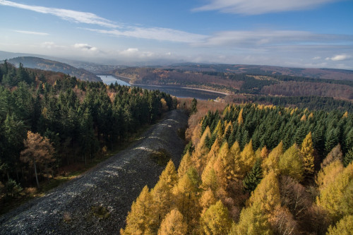 Luftbild von großem Steinwall mit herbstlichem Wald und Gewässer im Hintergrund