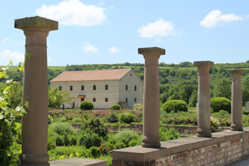 Blick auf großes Haus in Gartenanlage mit Säulen im Vordergrund